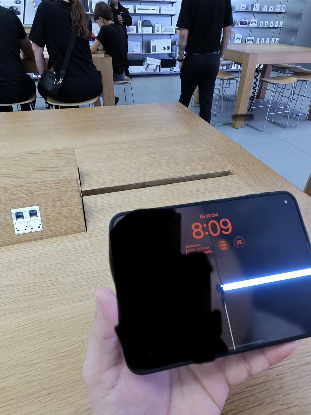 澳洲使用者手持 iPhone Duo，內螢幕沿中央摺痕一道縱向裂線，右半部橫向亮起一條白線